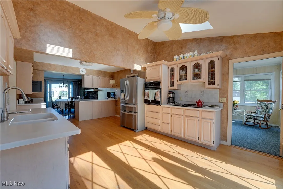 Kitchen with light wood-type flooring, stainless steel fridge with ice dispenser, oven, glass insert cabinets, and a towering ceiling
