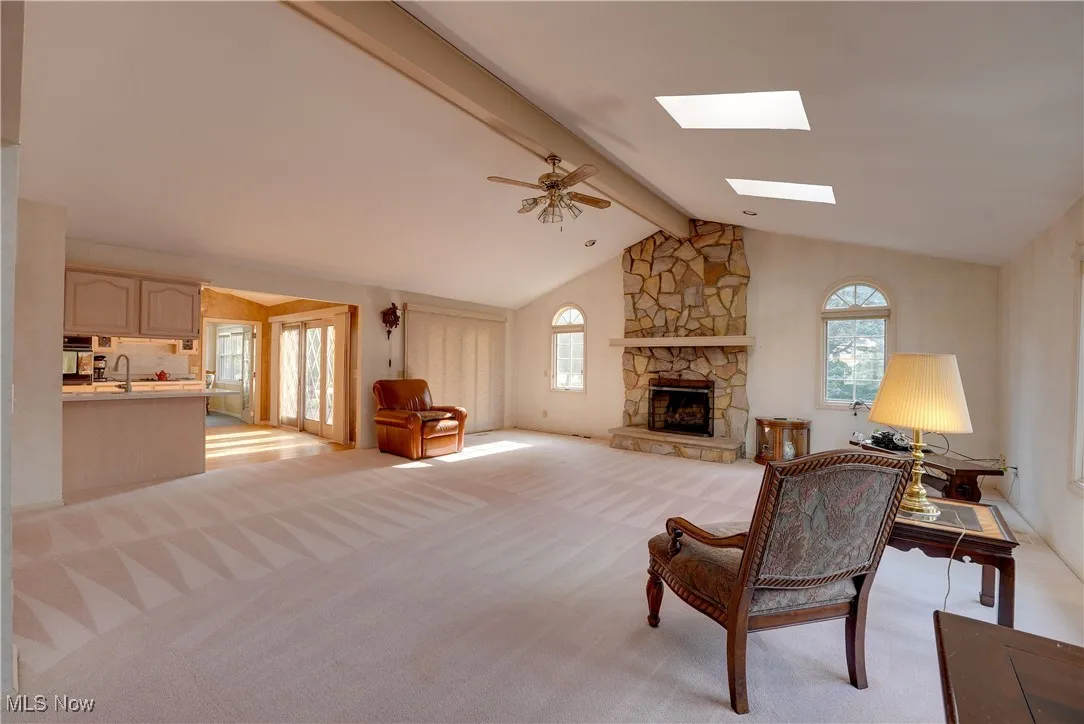 Great room featuring beam ceiling, healthy amount of natural light,a stone fireplace, and high vaulted ceiling
