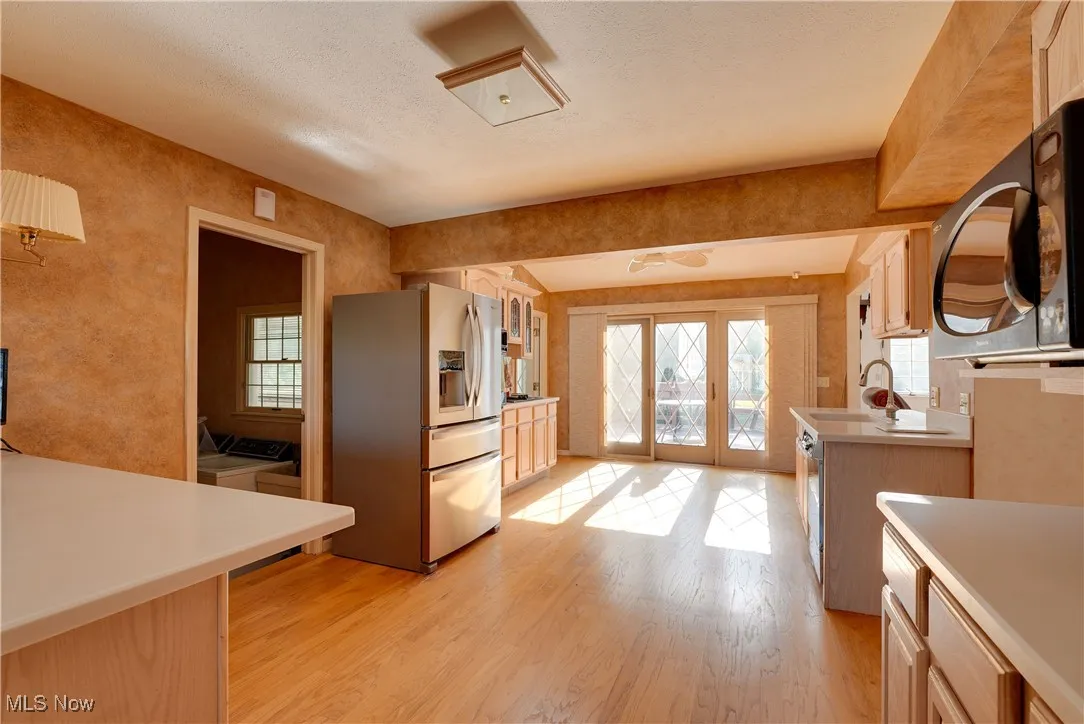 Kitchen featuring stainless steel refrigerator, light wood-style floors, light countertops, plenty of natural light.