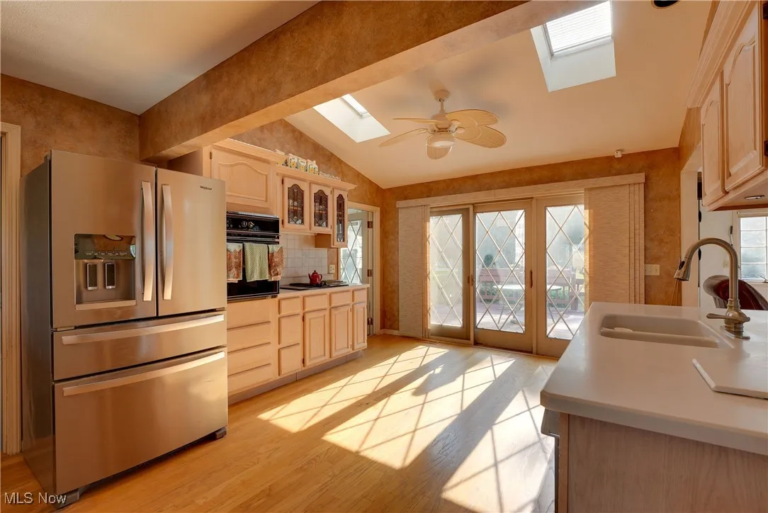 Kitchen with a skylight, stainless steel refrigerator with ice dispenser, vaulted ceiling, light brown cabinets, and light wood-style flooring