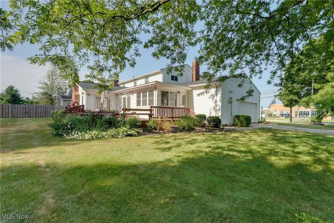 Rear view of property featuring a chimney, a wooden deck, driveway, and an attached garage