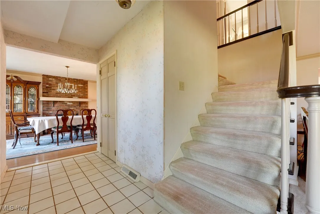 Stairs featuring wallpapered walls, tile patterned flooring, and a chandelier