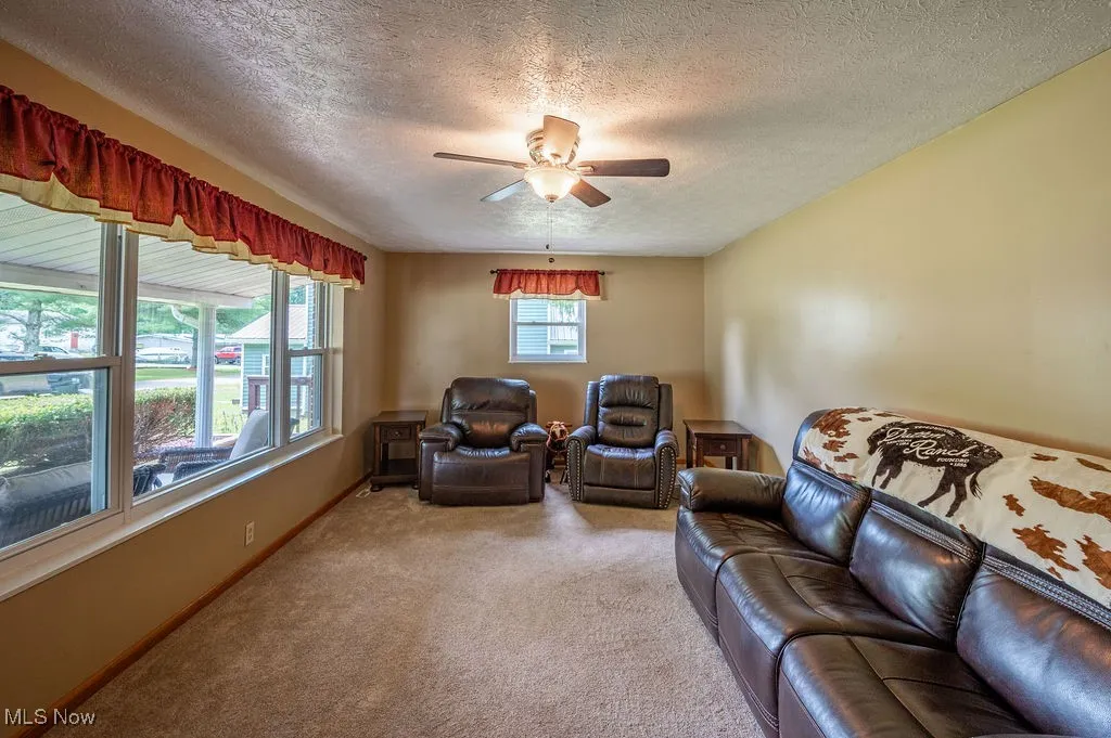 Carpeted living area featuring a ceiling fan and a textured ceiling