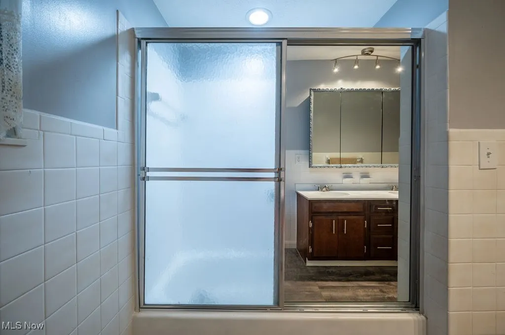 Full bathroom with tile walls, vanity, a shower with door, and a wainscoted wall
