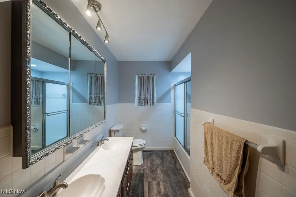 Bathroom with tile walls, wood finished floors, wainscoting, and double vanity