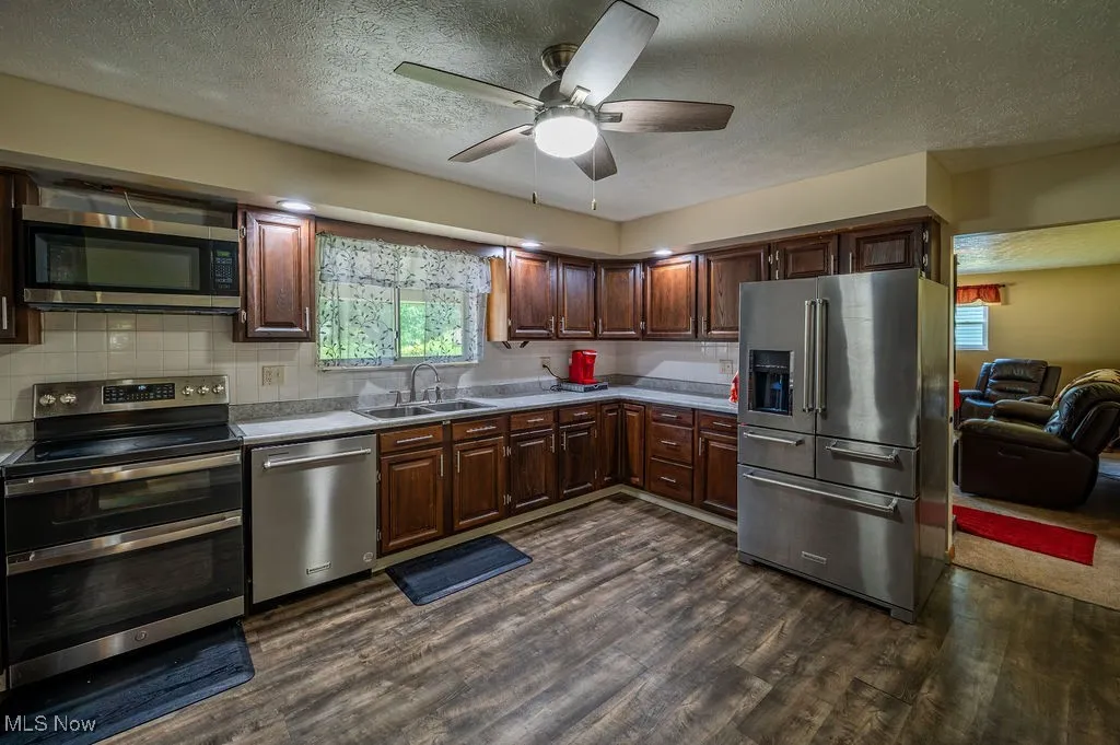 Kitchen with appliances with stainless steel finishes, dark wood finished floors, a textured ceiling, a ceiling fan, and decorative backsplash
