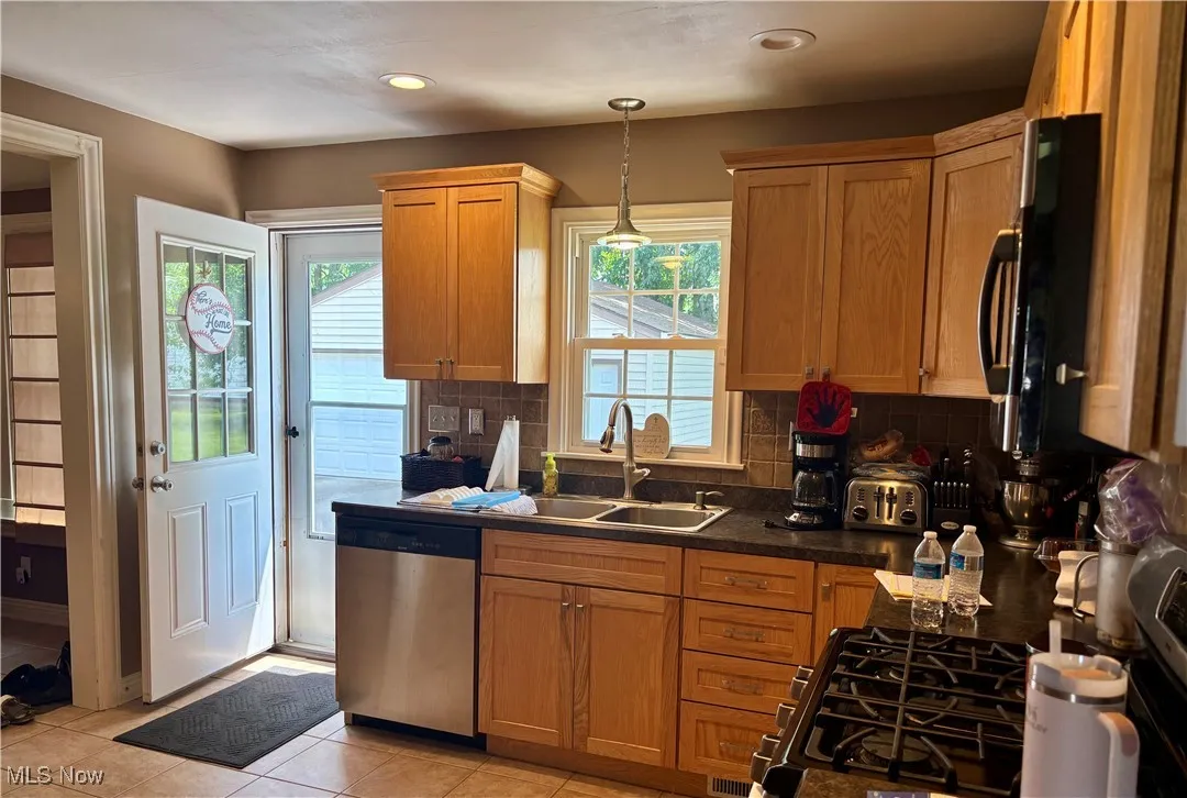 Kitchen with stove, dishwasher, decorative backsplash, black microwave, and plenty of natural light