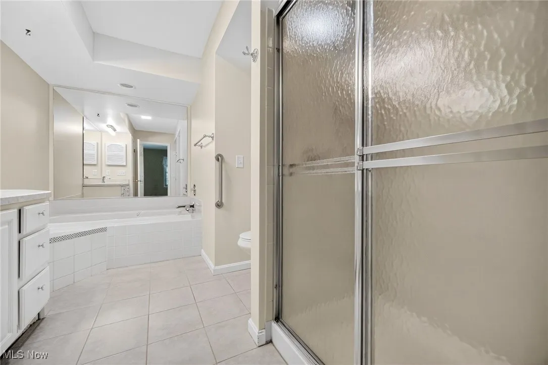 Bathroom featuring tile patterned flooring, vanity, a stall shower, and a relaxing tiled tub