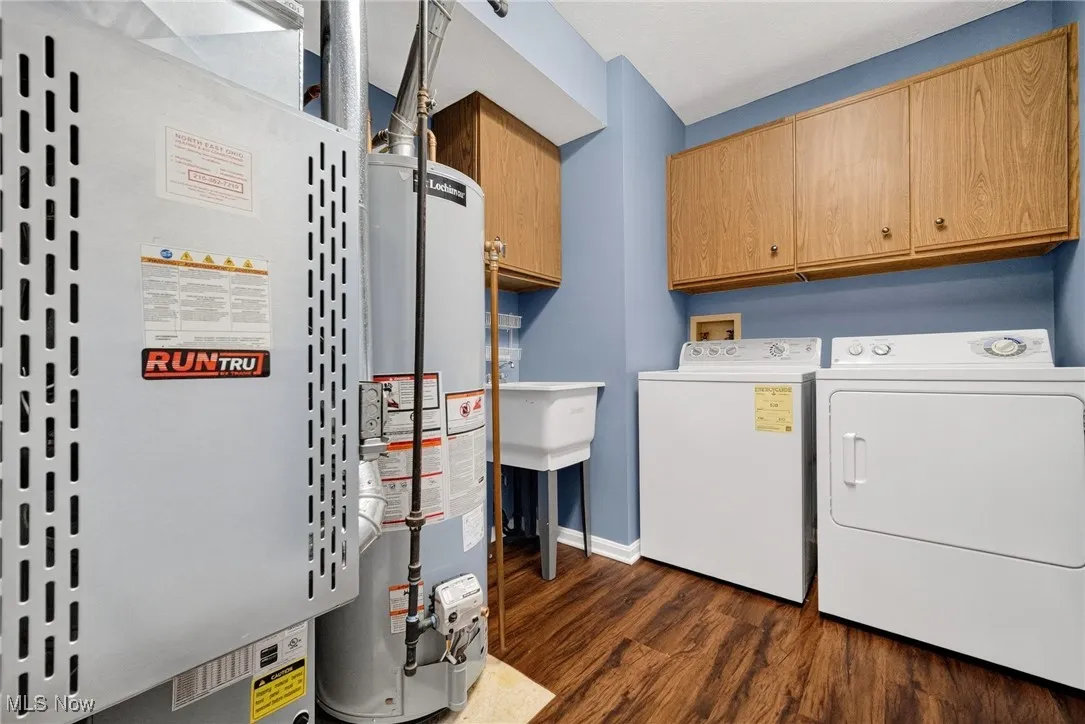 Laundry area featuring separate washer and dryer, cabinet space, heating unit, water heater, and dark wood finished floors