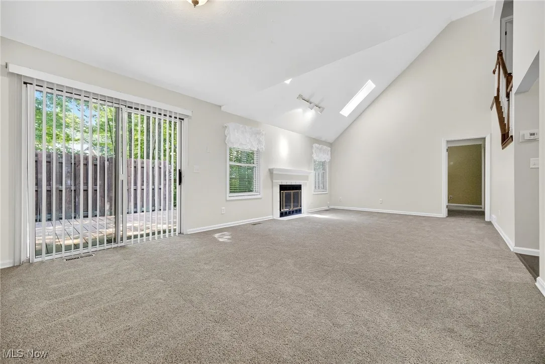 Unfurnished living room featuring carpet, a skylight, a fireplace, and high vaulted ceiling