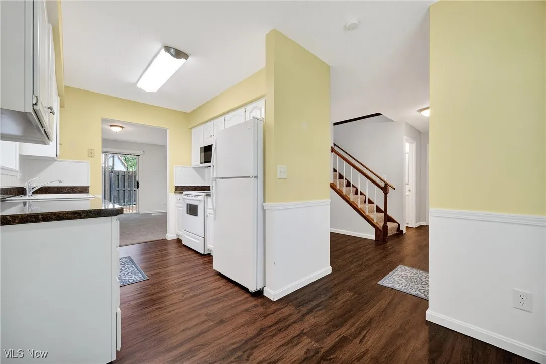 Kitchen with white appliances, white cabinetry, dark wood-type flooring, and dark countertops