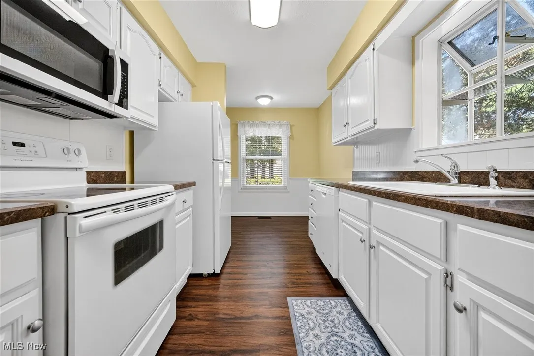 Kitchen with white appliances, dark wood-type flooring, white cabinetry, and dark countertops