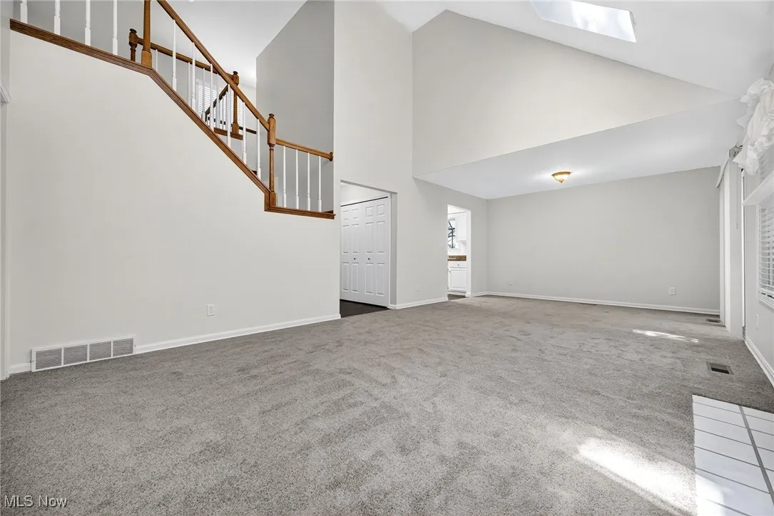 Unfurnished living room with high vaulted ceiling, carpet floors, stairway, and a skylight