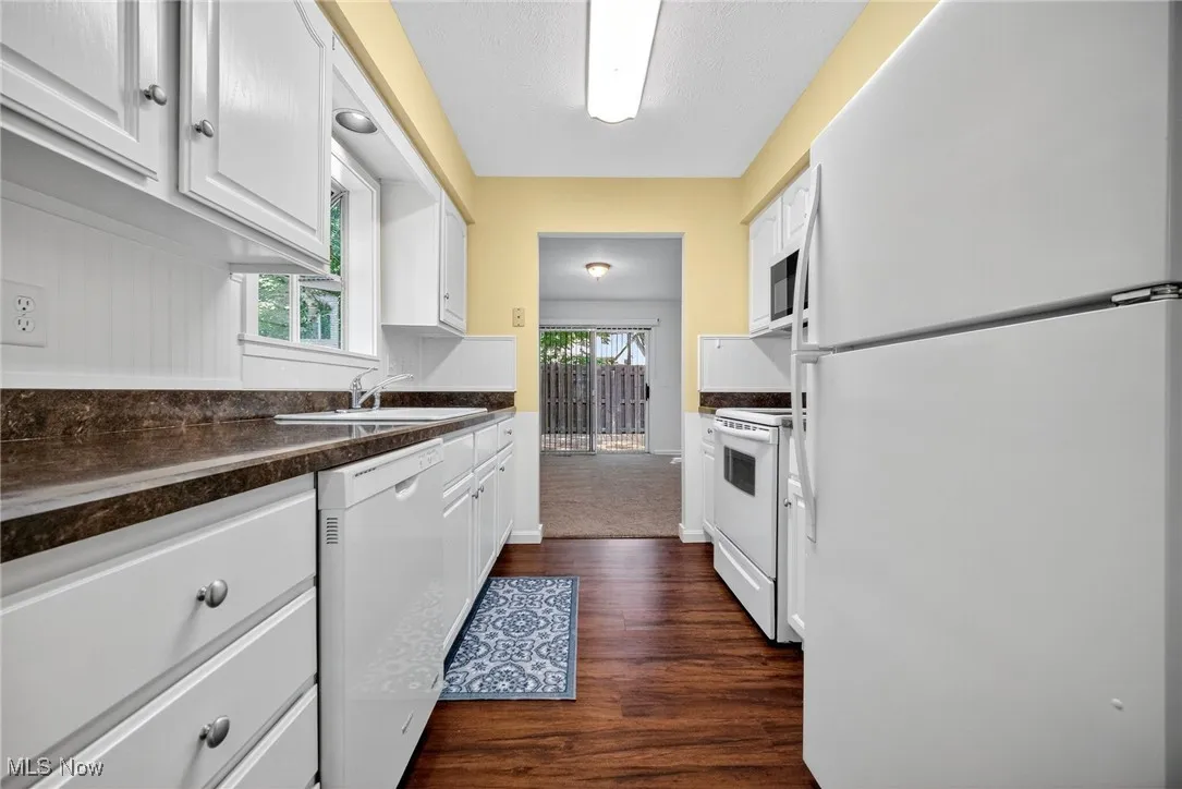Kitchen with white appliances, white cabinetry, dark wood-type flooring, and dark countertops