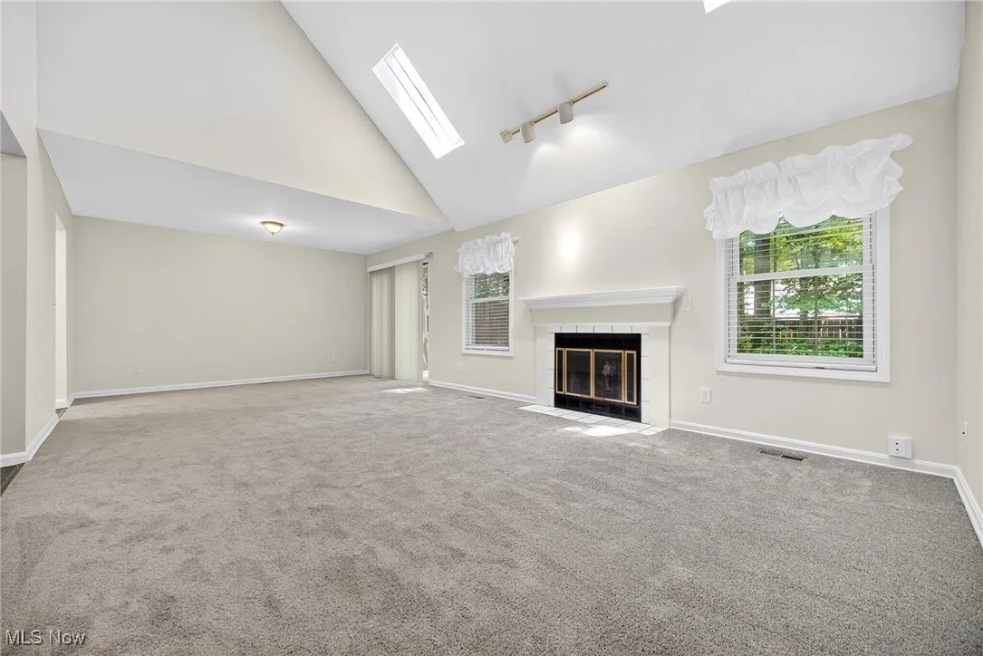 Unfurnished living room featuring a skylight, carpet, a tile fireplace, track lighting, and high vaulted ceiling