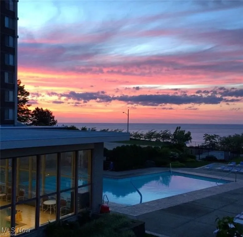 Pool at dusk featuring a water view, a community pool, and a patio