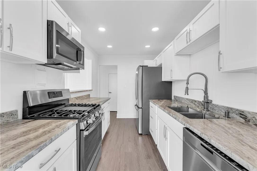 Kitchen featuring stainless steel appliances, white cabinets, light wood-style flooring, recessed lighting, and light stone counters