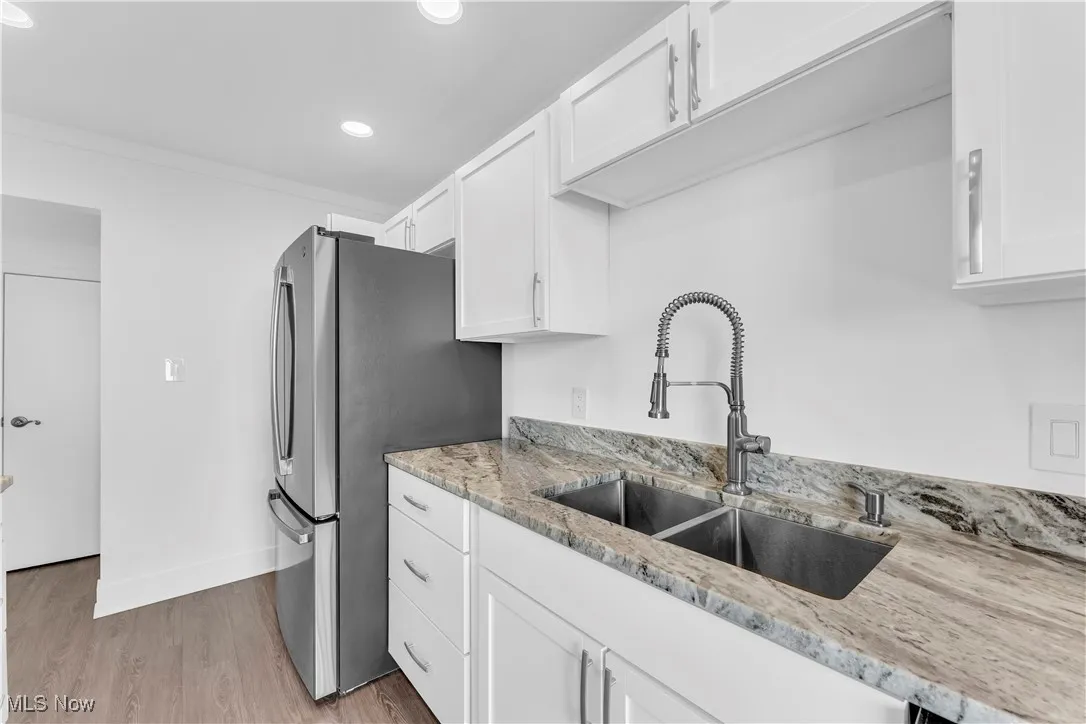 Kitchen with light wood-style floors, white cabinets, light stone counters, and recessed lighting