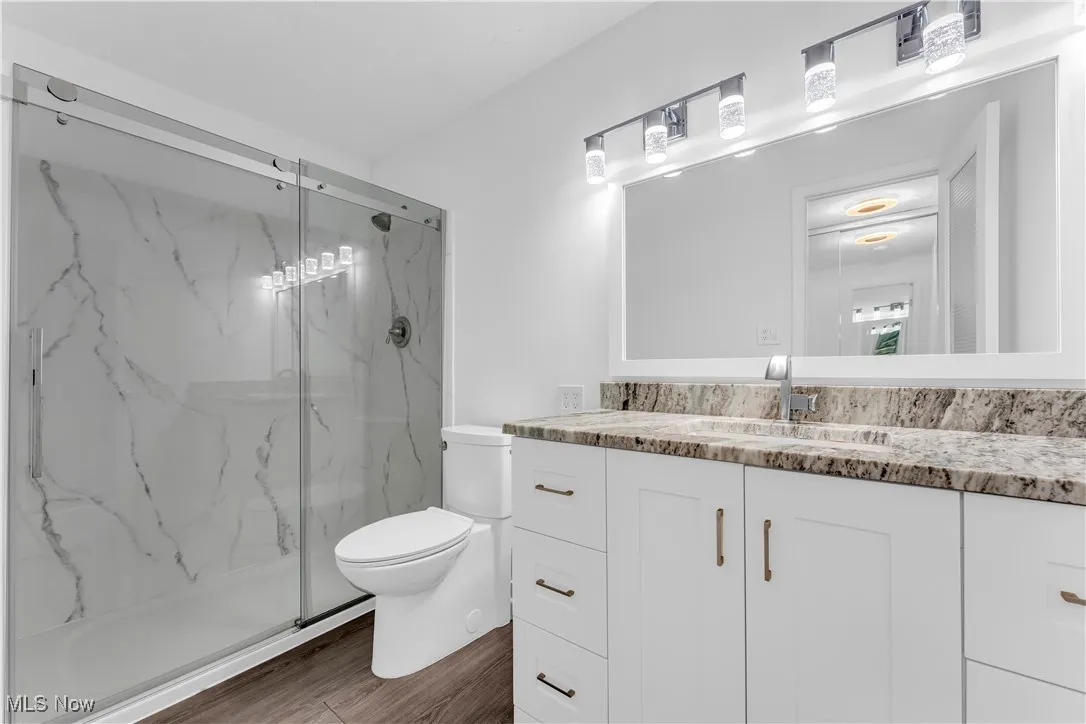 Full bath featuring vanity, a marble finish shower, and wood finished floors