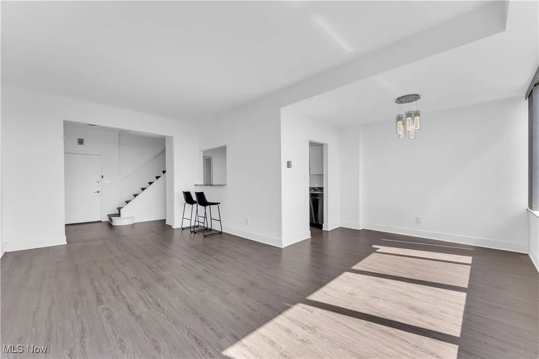 Unfurnished living room featuring stairs, a chandelier, and wood finished floors