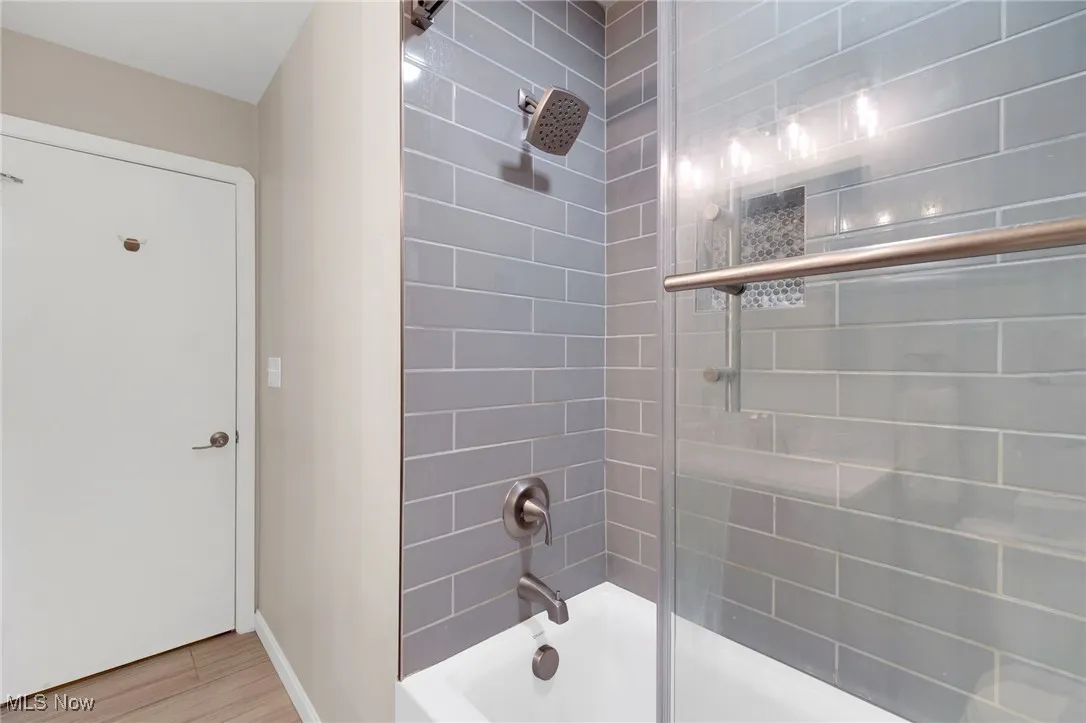 Full bathroom with bath / shower combo with glass door and wood finished floors