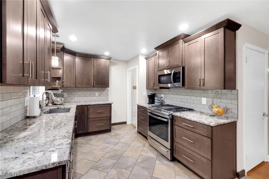 Kitchen with appliances with stainless steel finishes, decorative backsplash, light stone counters, recessed lighting, and dark brown cabinetry