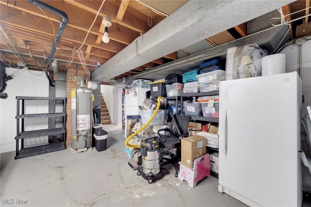 Unfinished basement featuring freestanding refrigerator, gas water heater, and stairs