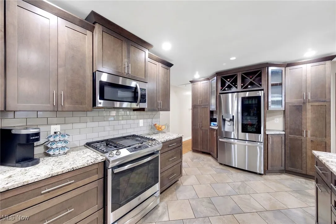 Kitchen with appliances with stainless steel finishes, tasteful backsplash, recessed lighting, light stone countertops, and glass insert cabinets