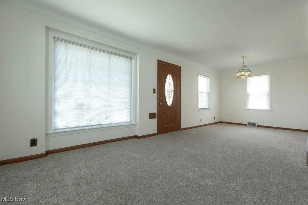 Carpeted entryway featuring a chandelier and baseboards