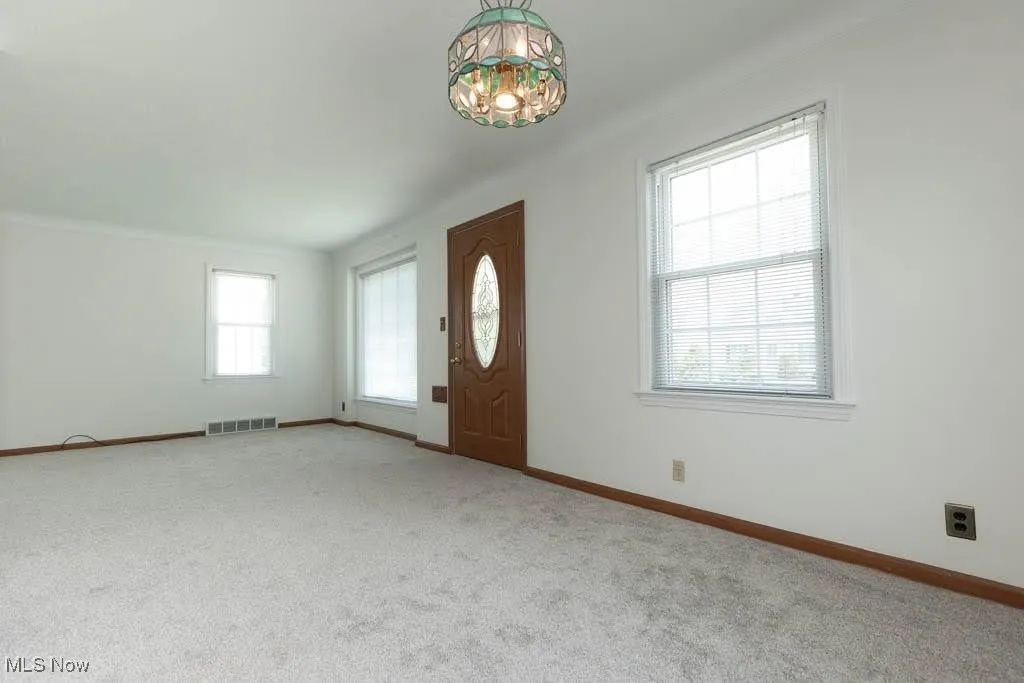 Carpeted foyer entrance with a chandelier and baseboards