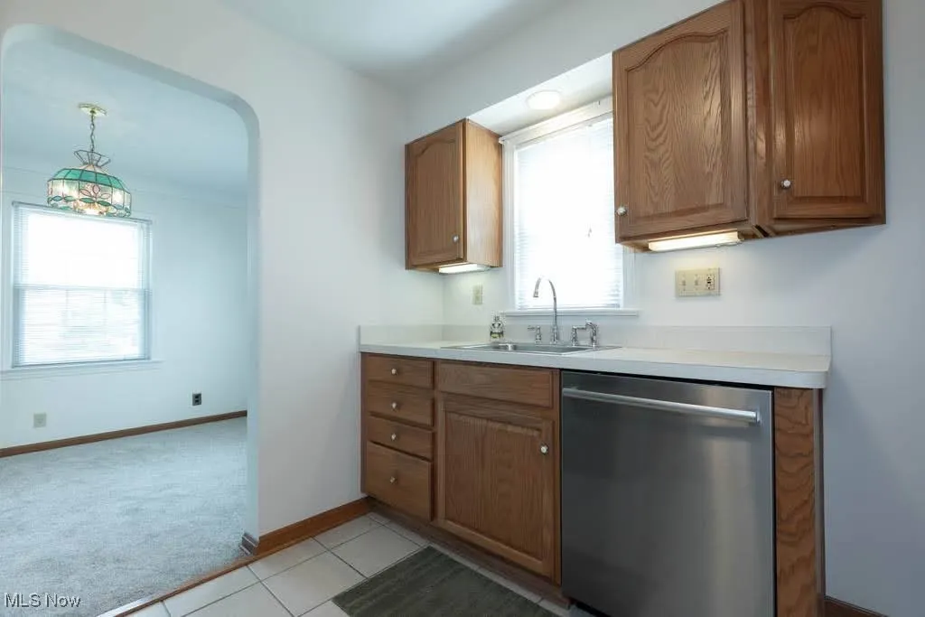 Kitchen featuring dishwasher, light countertops, light carpet, brown cabinetry, and pendant lighting
