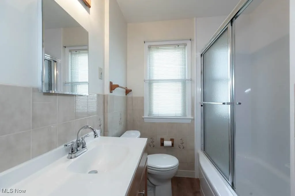 Full bath with vanity, tile walls, shower / bath combination with glass door, and a wainscoted wall