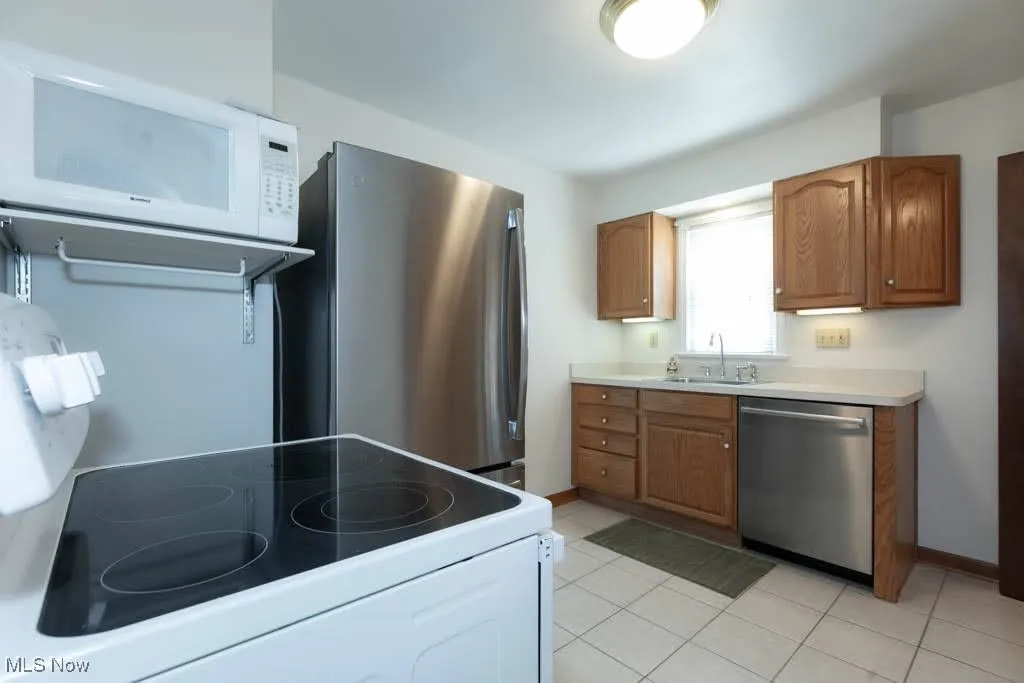 Kitchen with appliances with stainless steel finishes, brown cabinetry, light countertops, and light tile patterned floors