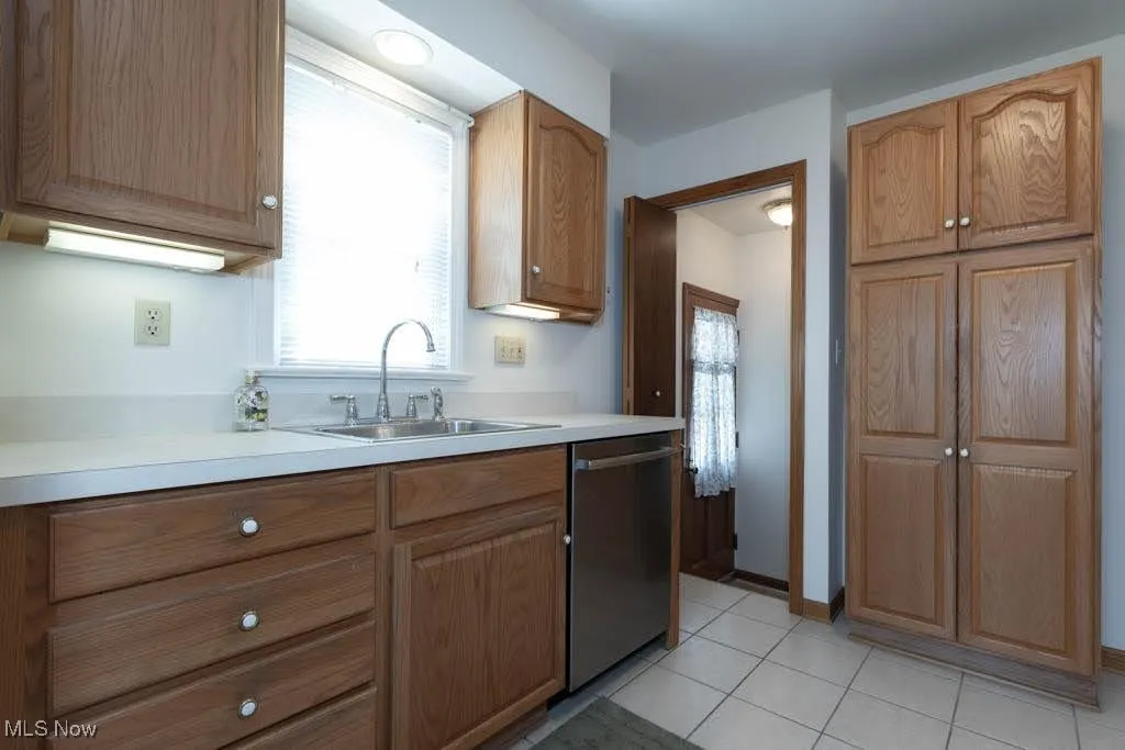 Kitchen featuring dishwasher, light countertops, light tile patterned floors, and brown cabinets