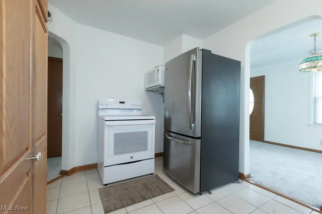 Kitchen featuring white appliances, arched walkways, and light tile patterned flooring