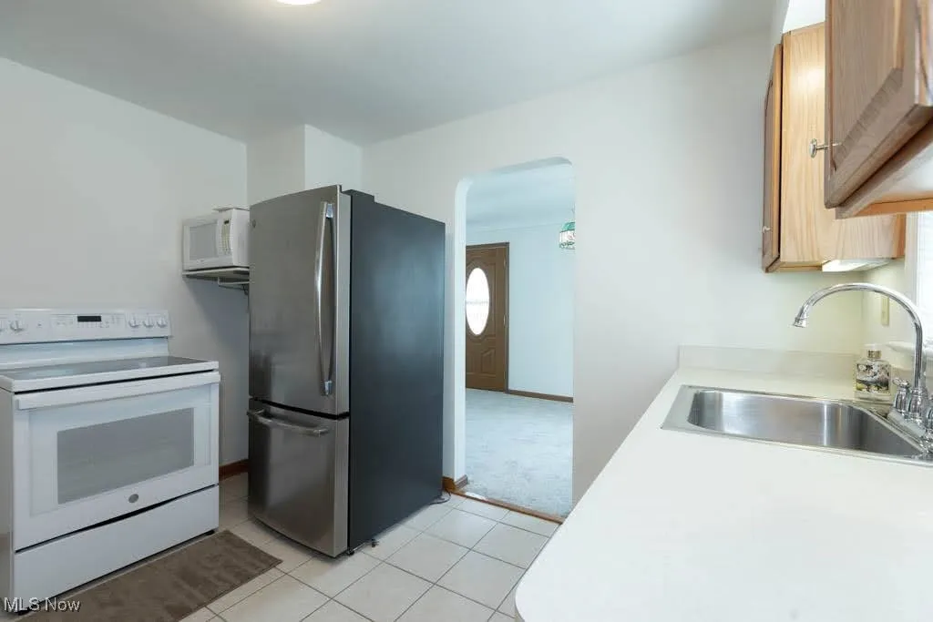 Kitchen featuring white appliances, arched walkways, light countertops, light tile patterned floors, and light colored carpet