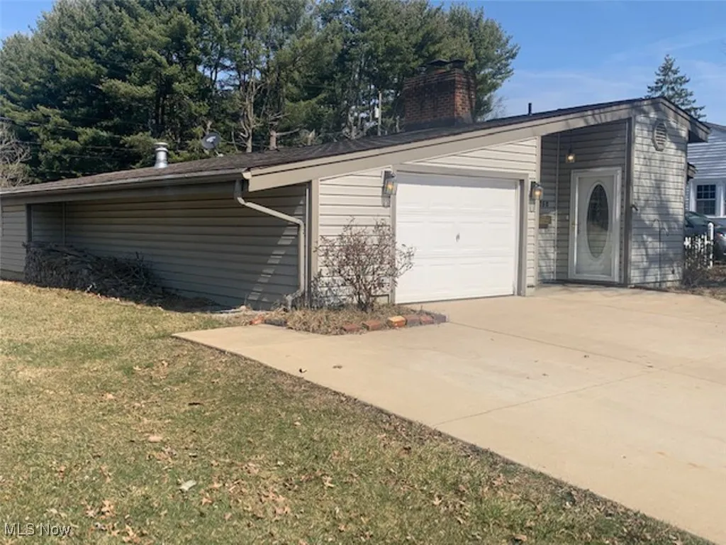 View of property exterior featuring driveway, a garage, a chimney, and a lawn