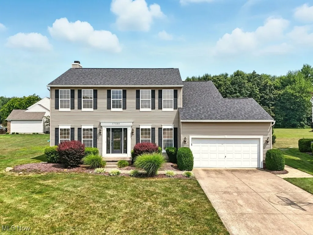 Colonial inspired home featuring a garage, a front lawn, concrete driveway, a chimney, and a shingled roof