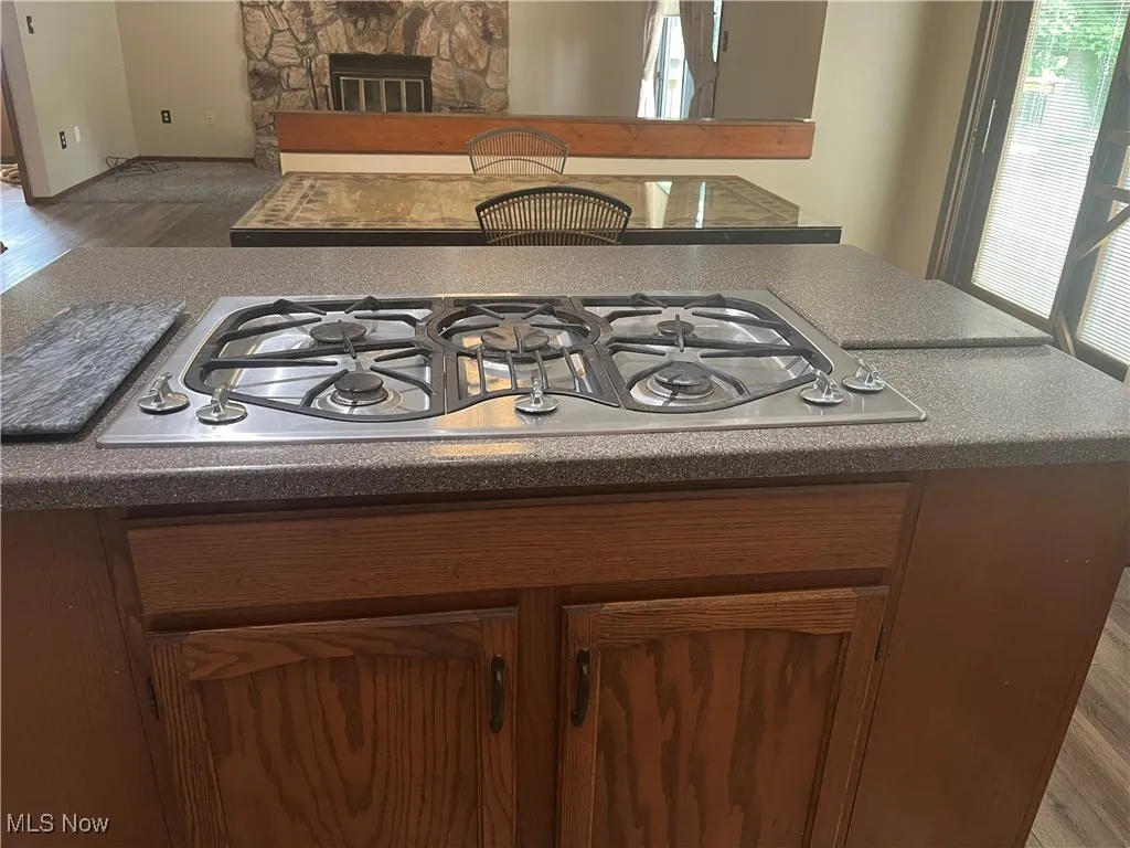 Stainless steel gas cooktop, wood finished floors, and brown cabinets