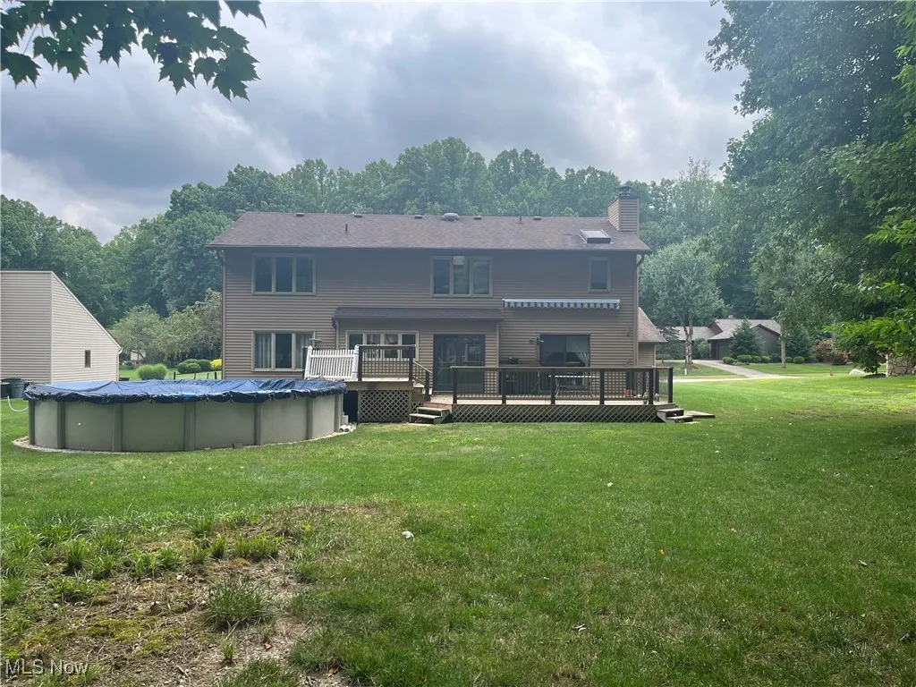 Rear view of house with above ground pool, 2-tiered wooden deck and a retractable awning.
