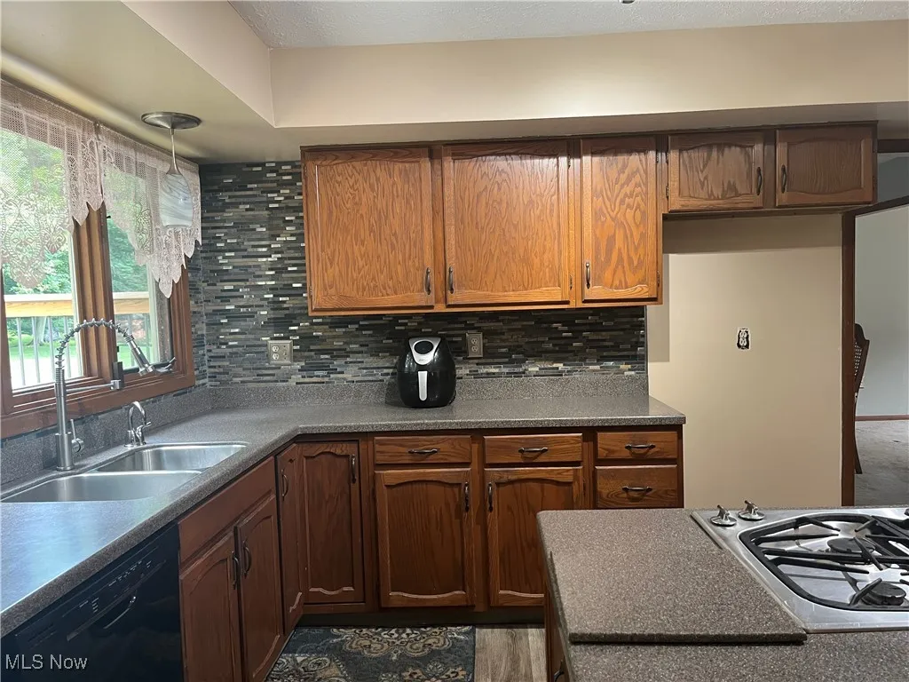 Kitchen with black dishwasher, gas cooktop, decorative backsplash, and lots of cabinets and countertop space.