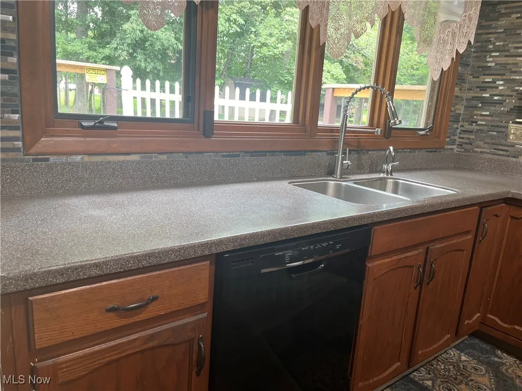 Kitchen with black dishwasher, healthy amount of natural light, and brown cabinets.