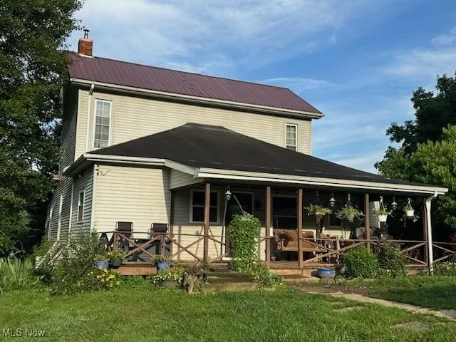 Rear view of property featuring a chimney, a porch, a metal roof, and a lawn