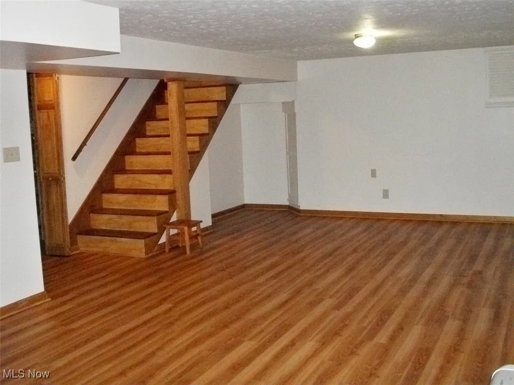Finished basement with light wood-style flooring, stairway, and a textured ceiling