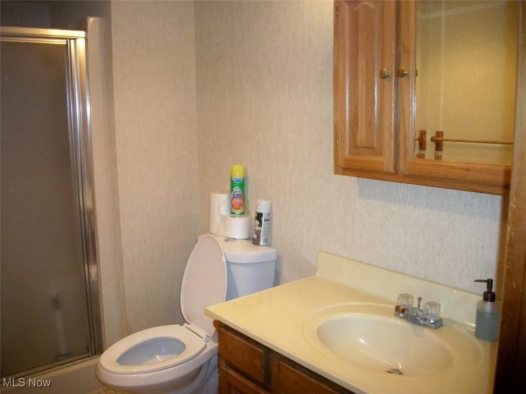 Bathroom with a shower stall, vanity, and wallpapered walls