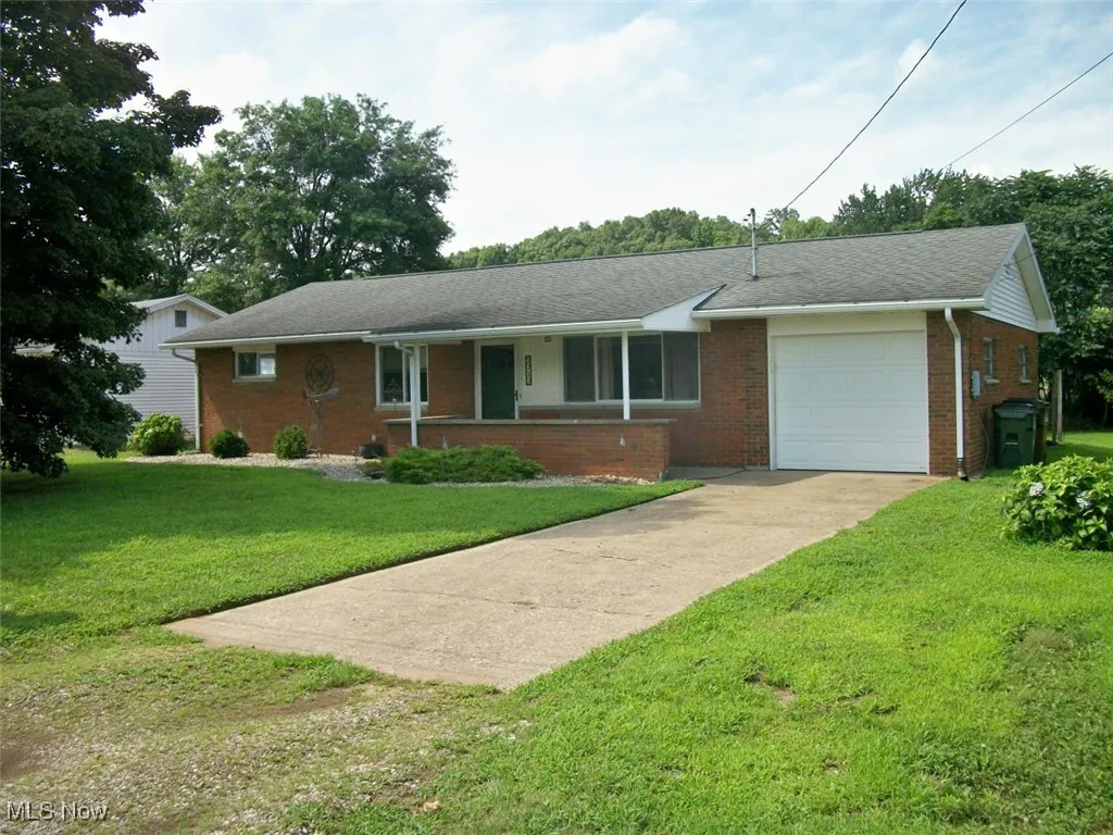 Single story home featuring a garage, concrete driveway, brick siding, a front lawn, and a shingled roof