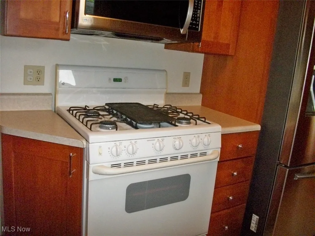 Kitchen with stainless steel appliances, brown cabinets, and light countertops