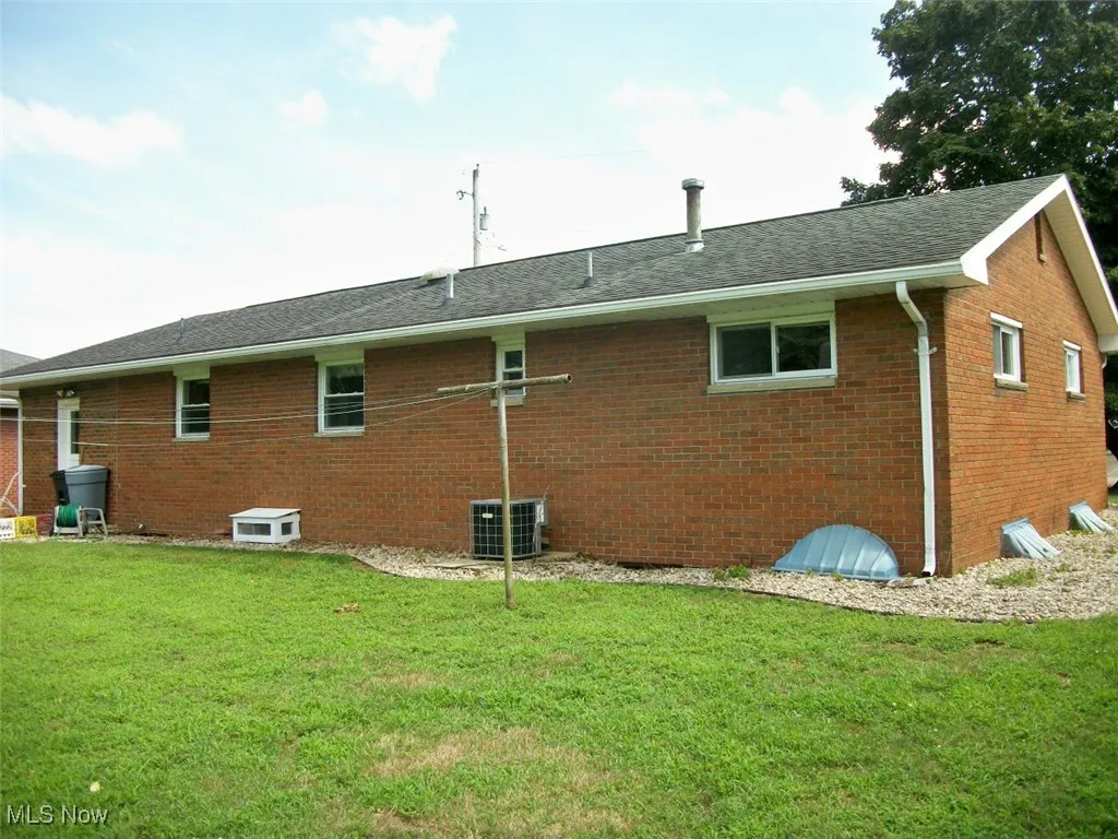 Rear view of house with brick siding, a yard, and roof with shingles