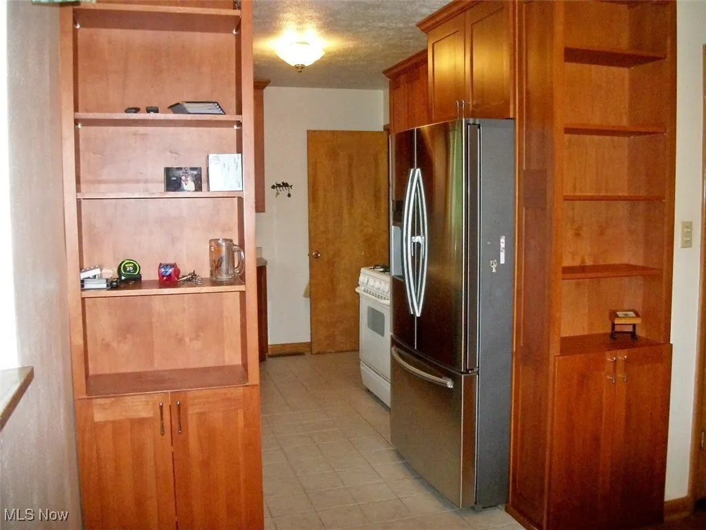 To the Heart of the home with book shelves, stainless steel fridge, white gas range oven, brown cabinets.