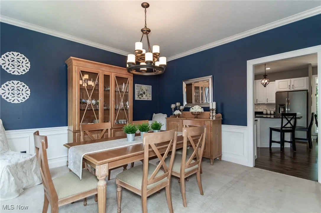 Dining room featuring a chandelier, crown molding, a wainscoted wall, and light carpet